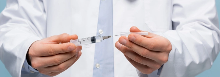 Close-up of a person in a white medical coat holding a syringe