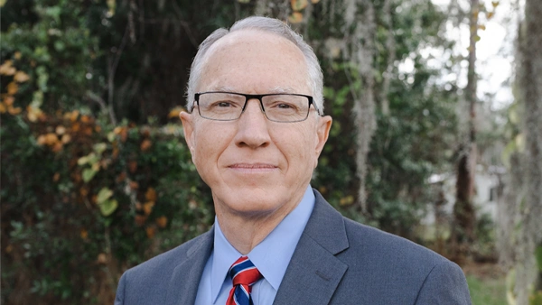 Dr. Keatley Waldron wearing glasses, a suit, and a striped tie, photographed outdoors