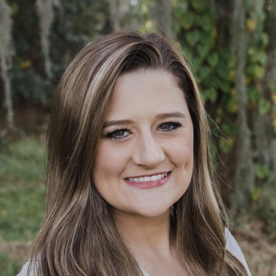 Dr. McKenna Cobb with long hair, smiling slightly, photographed against a background of trees